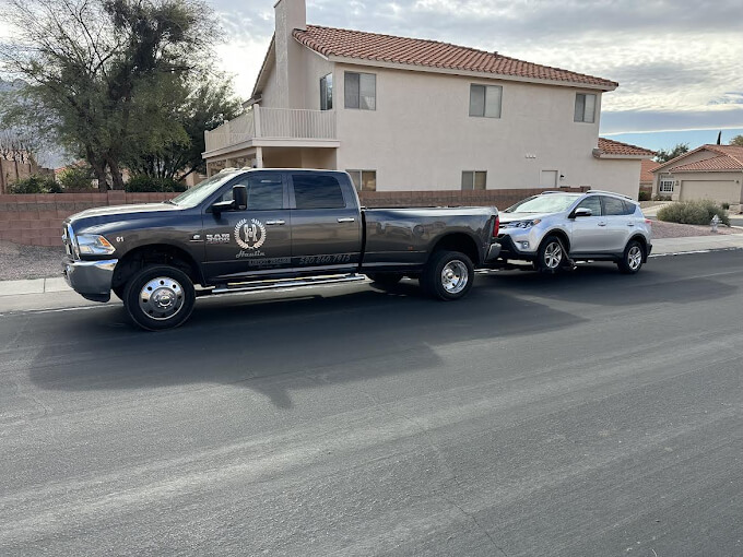 A large pickup truck towing a smaller SUV parked in front of a residential building.